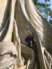 Person posing among the massive roots of a large tree