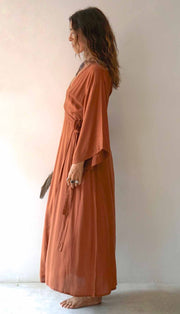 Woman wearing a long, rust-colored dress against a plain background