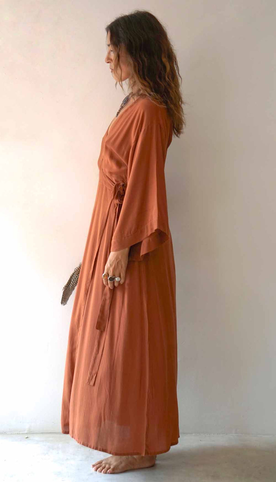 Woman wearing a long, rust-colored dress against a plain background
