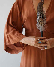 Person wearing a rust-colored dress holding a decorative item with feathers against a plain background