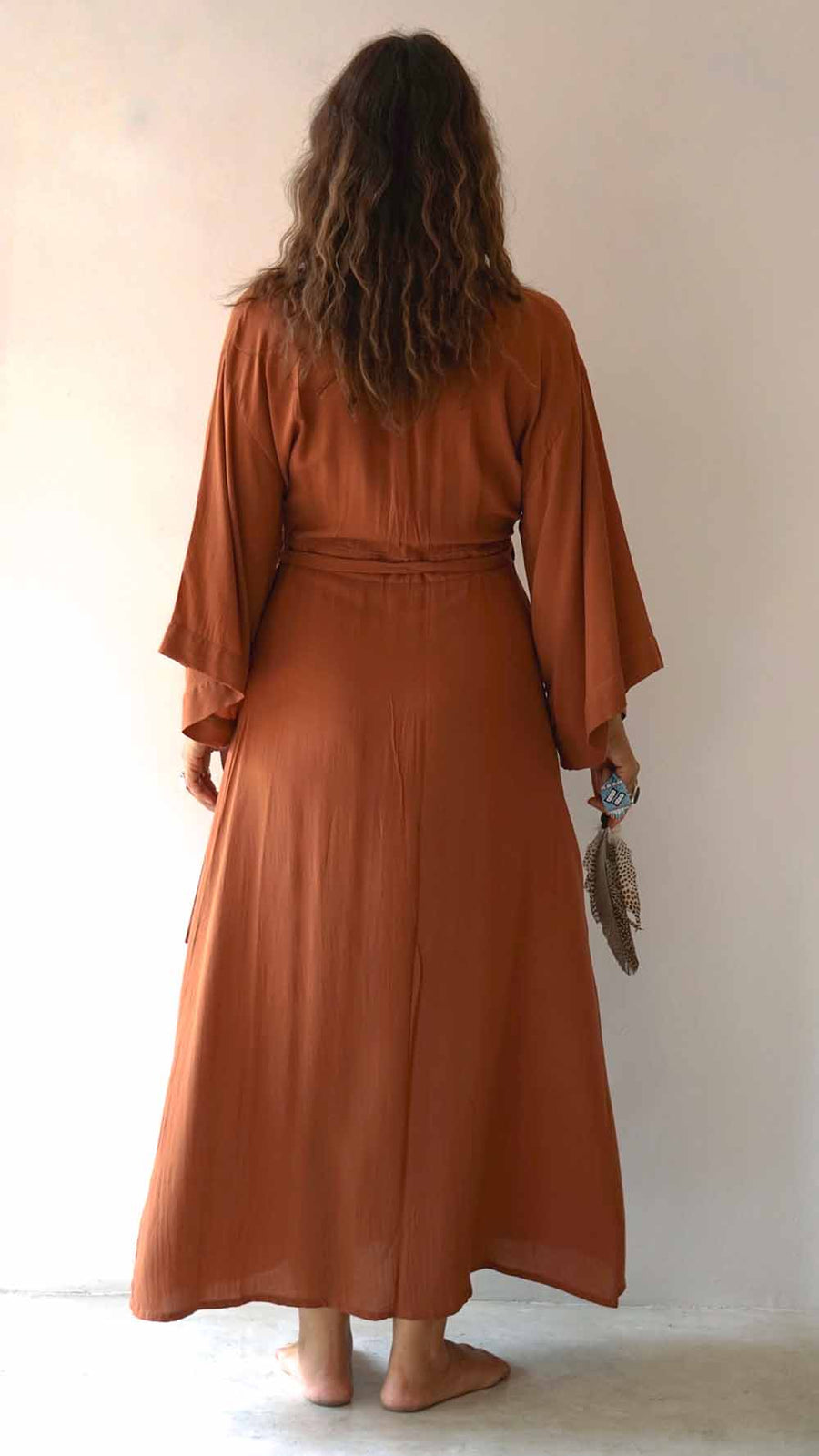 Person wearing a long rust-colored dress holding a feather against a plain background