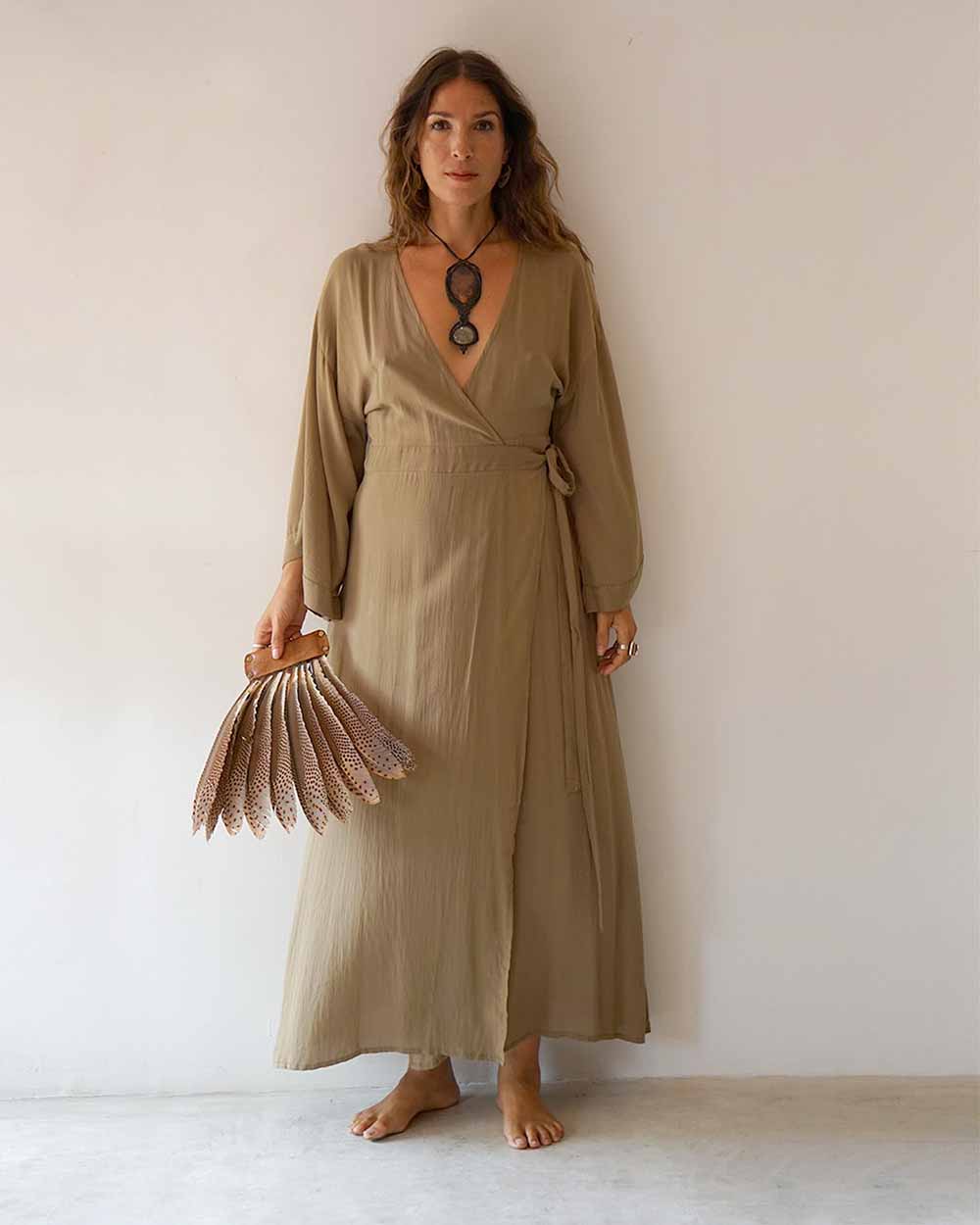 Woman wearing a long beige dress holding a fan against a plain background