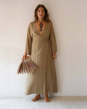 Woman wearing a long beige dress holding a fan against a plain background