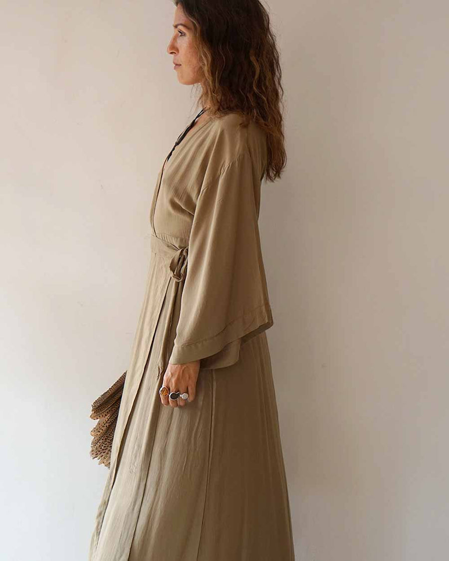 Woman wearing a long beige dress against a plain background