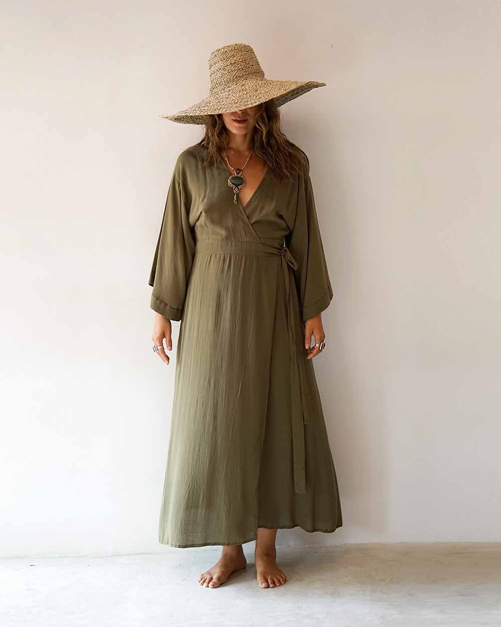 Woman wearing an olive green dress and wide-brimmed hat against a white background