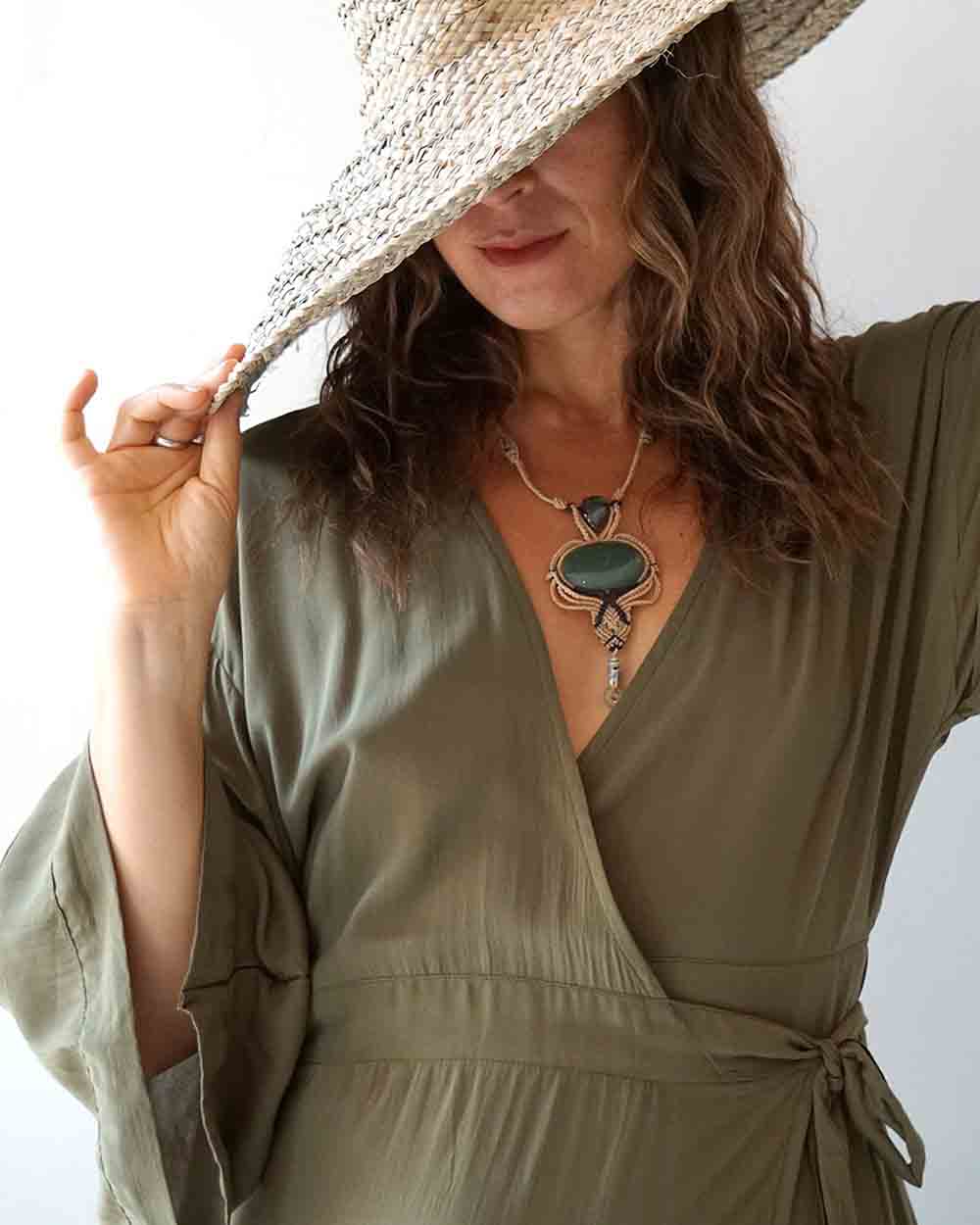 Woman wearing a green dress and straw hat with a necklace featuring a large pendant.