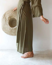 Person wearing a long olive green dress holding a straw hat on a white background