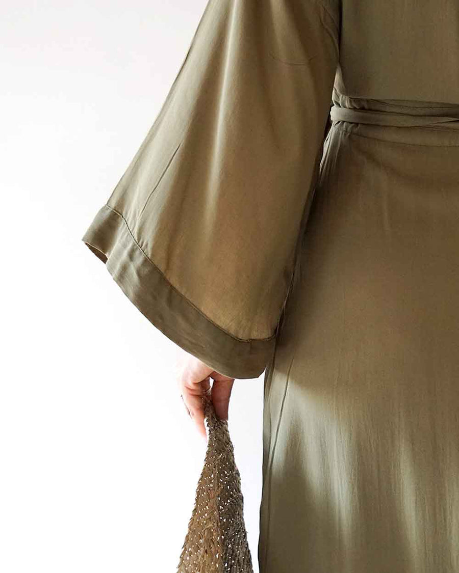 Close-up of a person wearing a beige trench coat holding a textured beige scarf.
