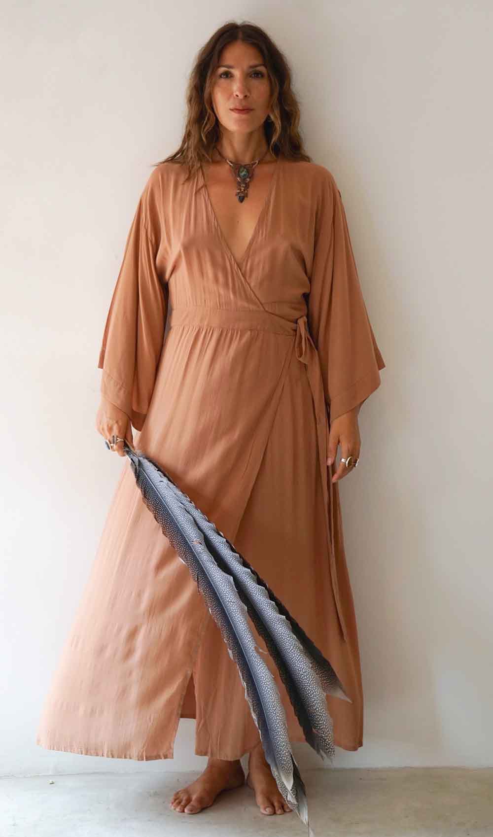 Woman wearing a long, light brown dress holding a blue scarf against a white background