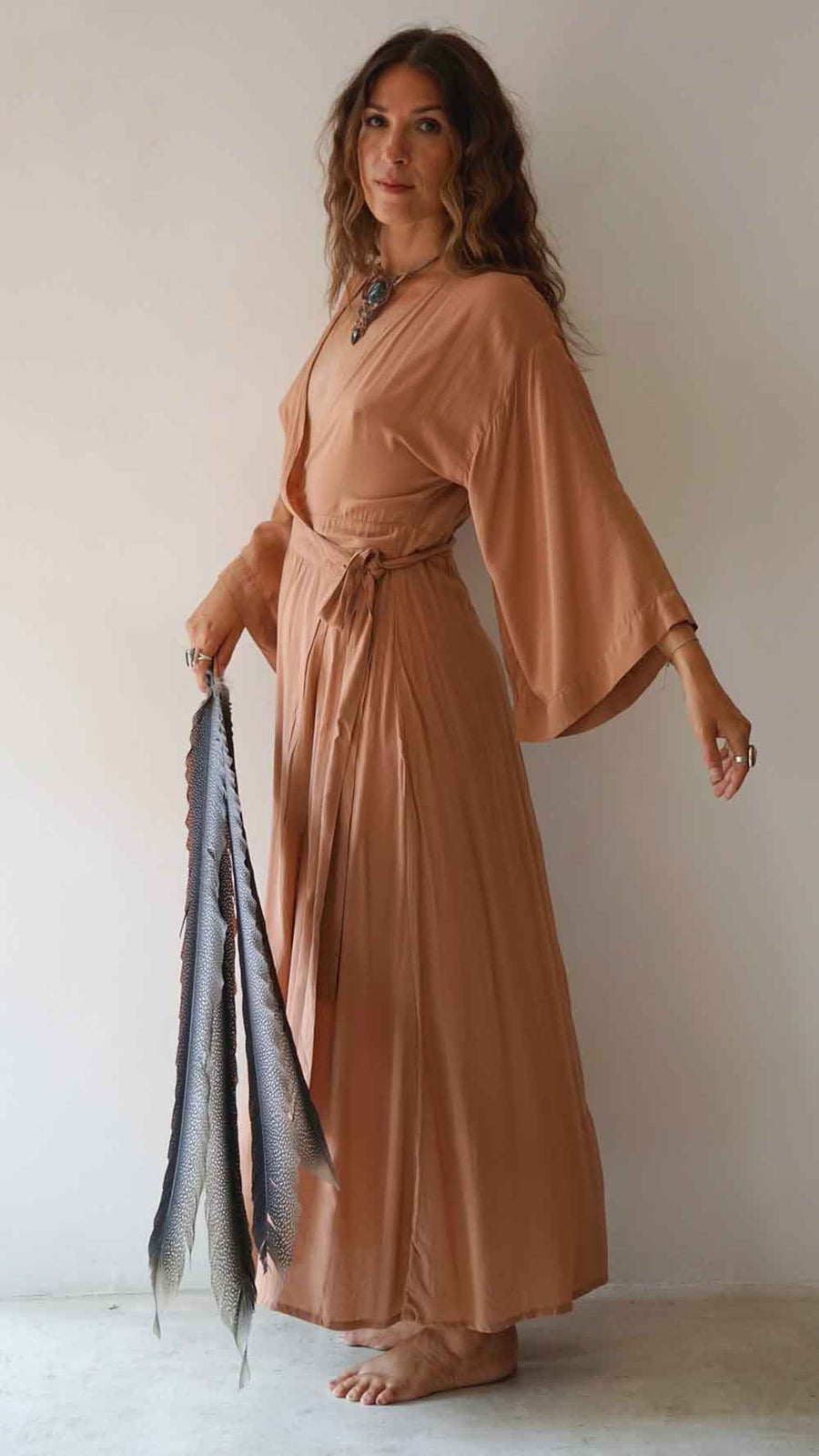 Woman wearing a long, flowing dress holding a scarf against a plain background