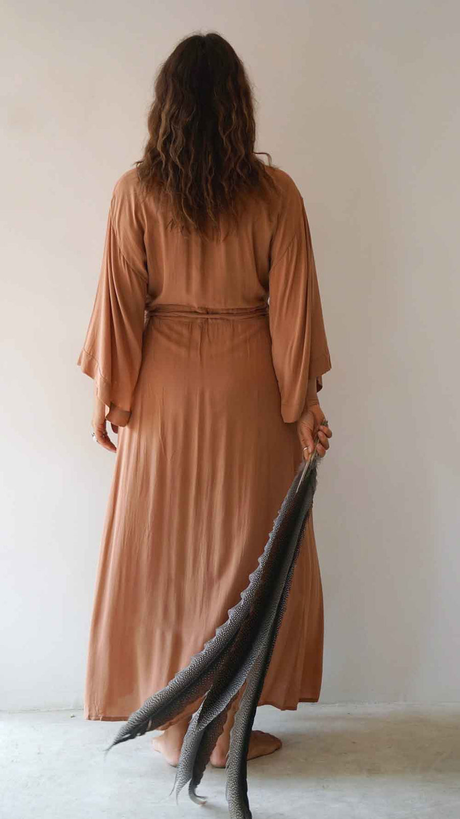 Woman wearing a long brown dress holding a black and gray scarf against a plain background