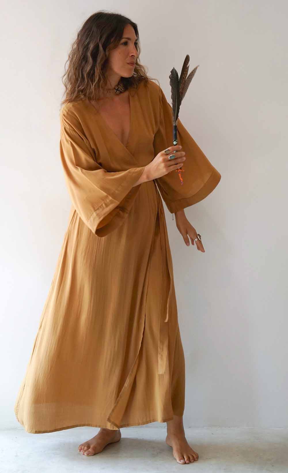 Woman in a long, light brown dress holding feathers against a white background