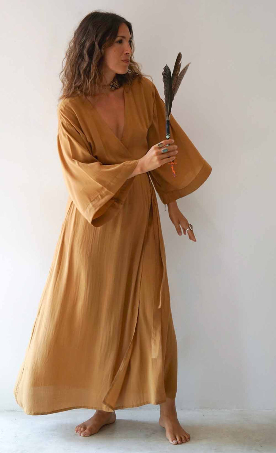 Woman in a long, light brown dress holding feathers against a white background