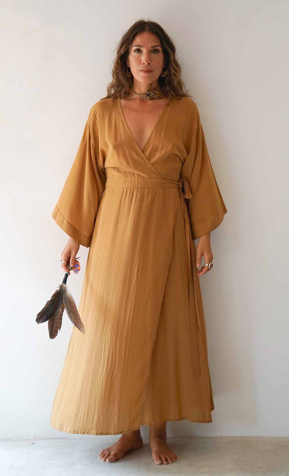 Woman wearing a mustard yellow dress holding a feathered object against a white background