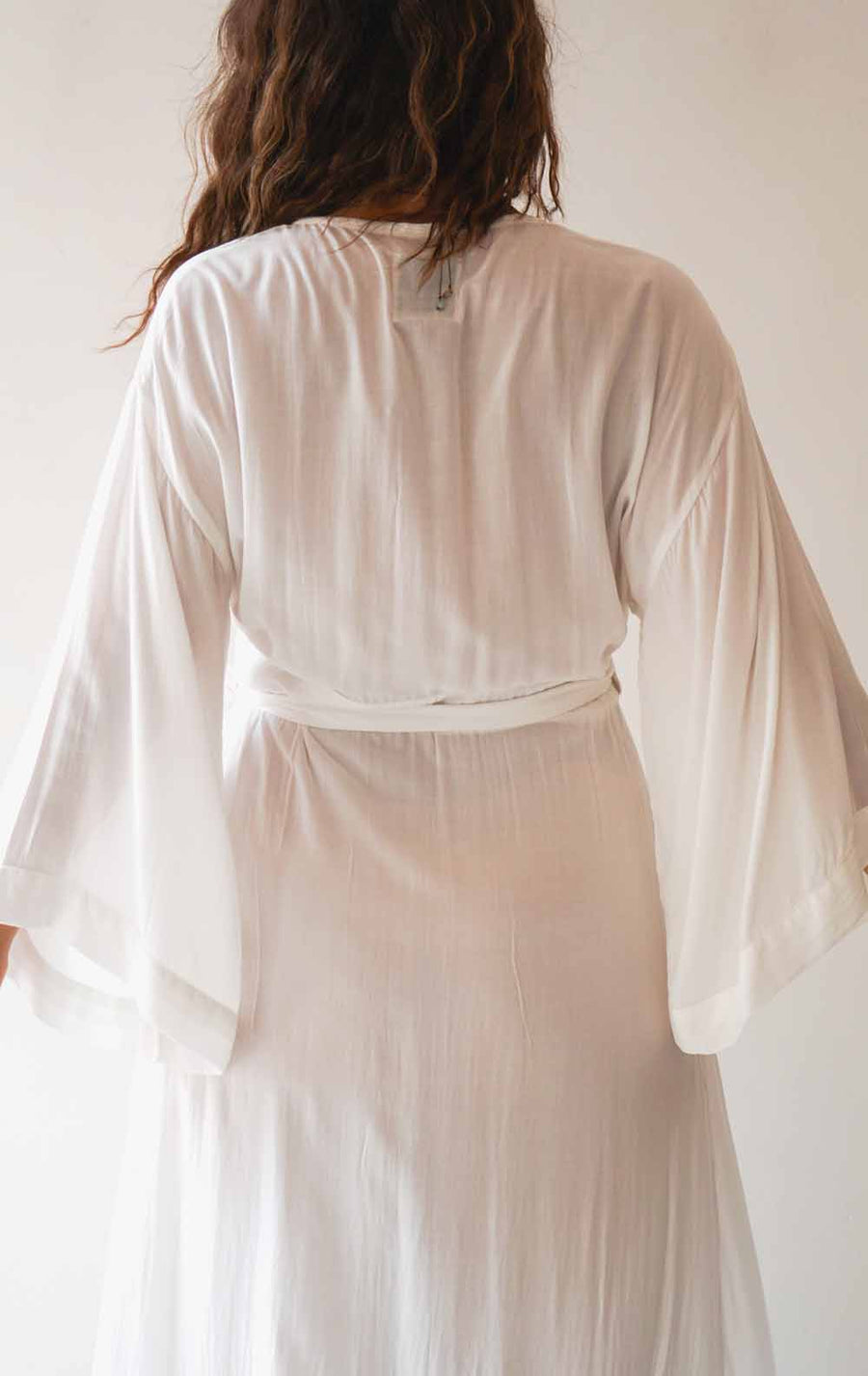 Person wearing a white dress with sheer sleeves against a plain background
