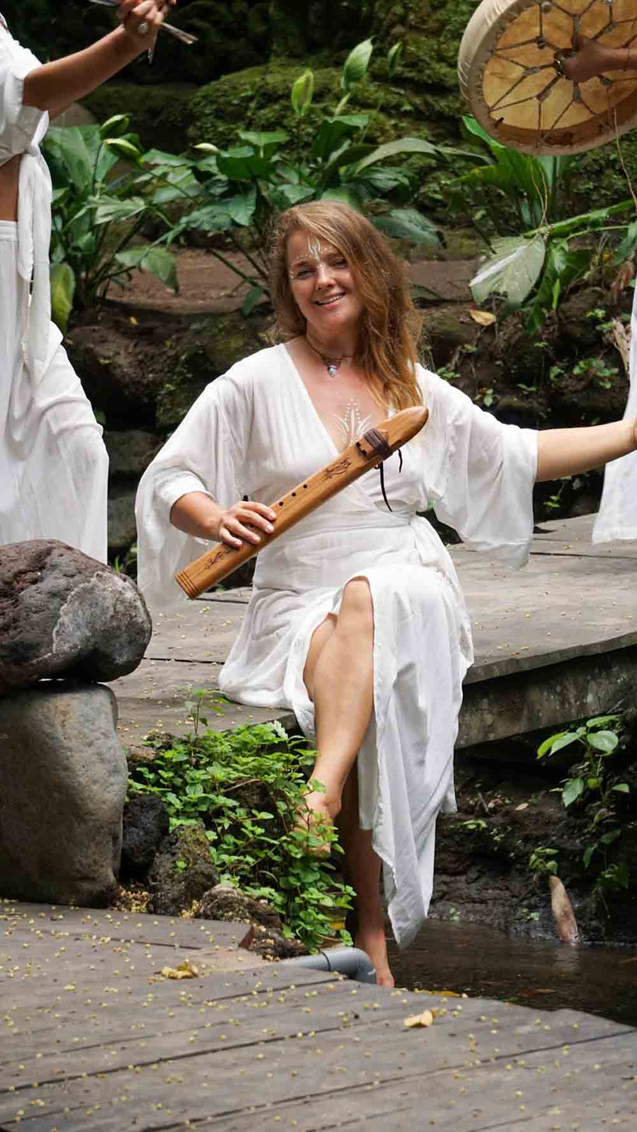 Woman in a white dress playing a wooden instrument in a natural setting