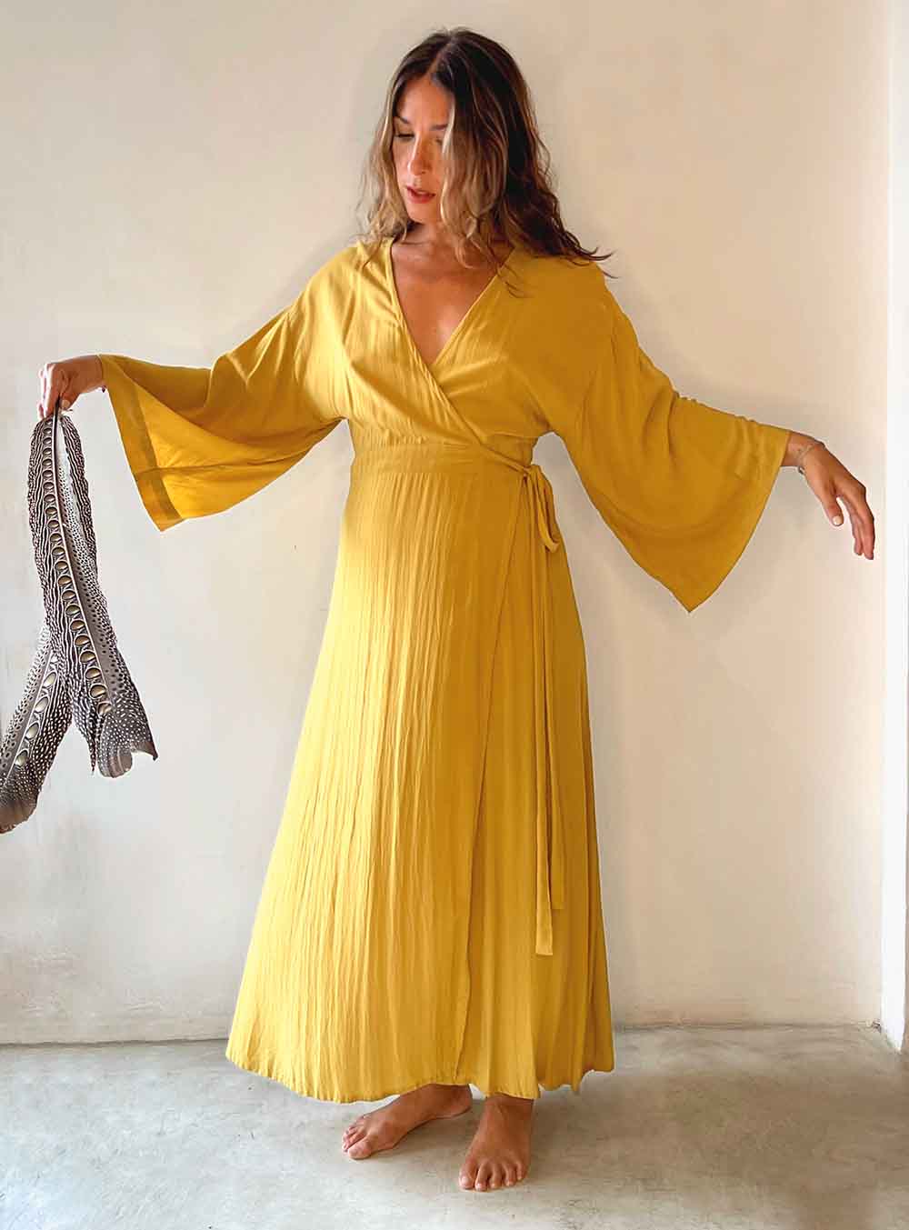 Woman wearing a yellow dress holding a feathered item against a plain background