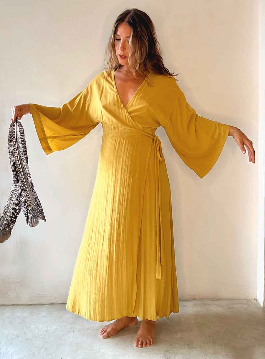 Woman wearing a yellow dress holding a feathered item against a plain background