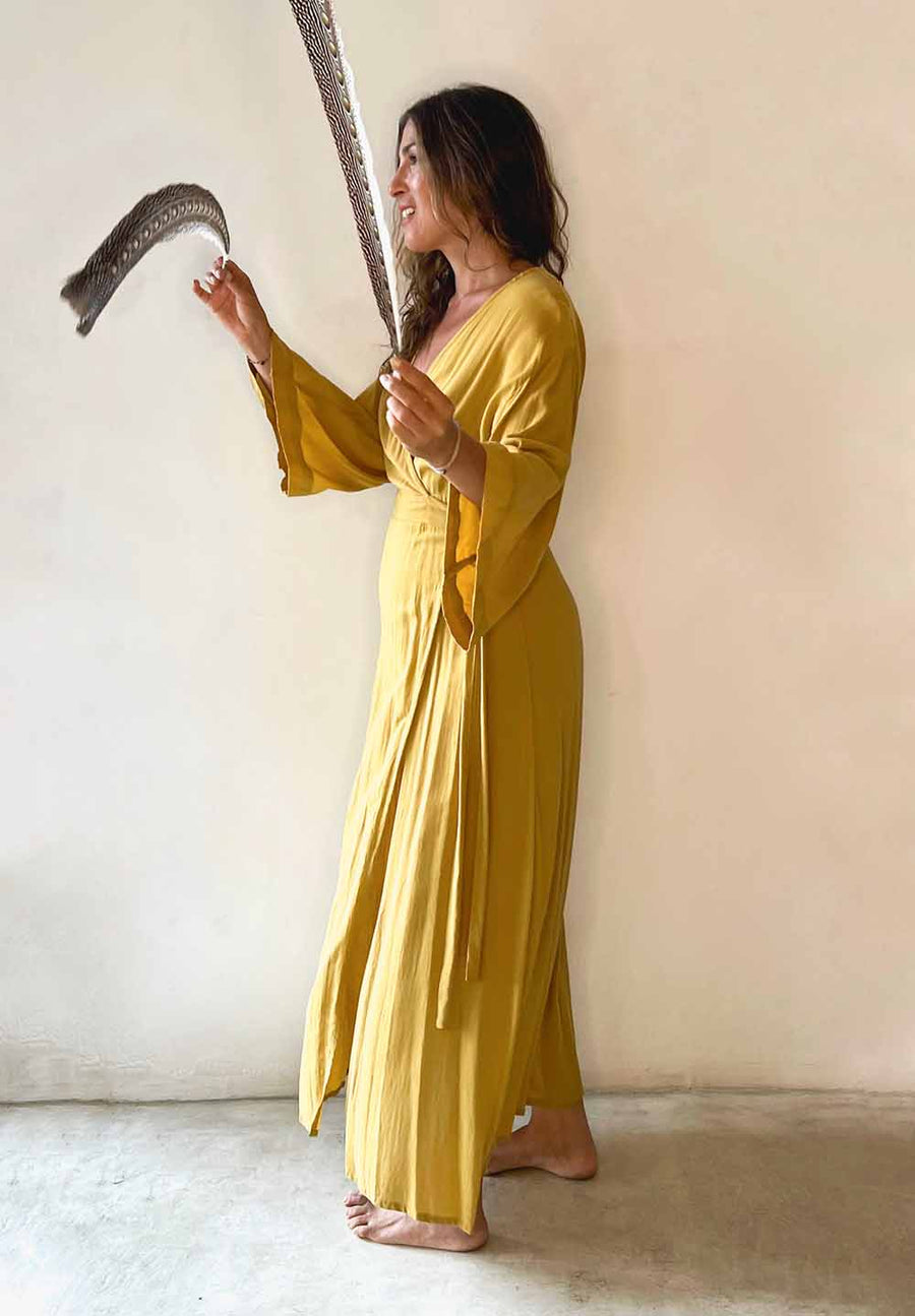 Woman in a yellow dress holding a black and silver object against a plain background