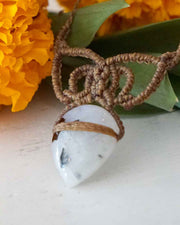 Macrame-wrapped stone pendant with a white stone on a light background with marigold flowers.