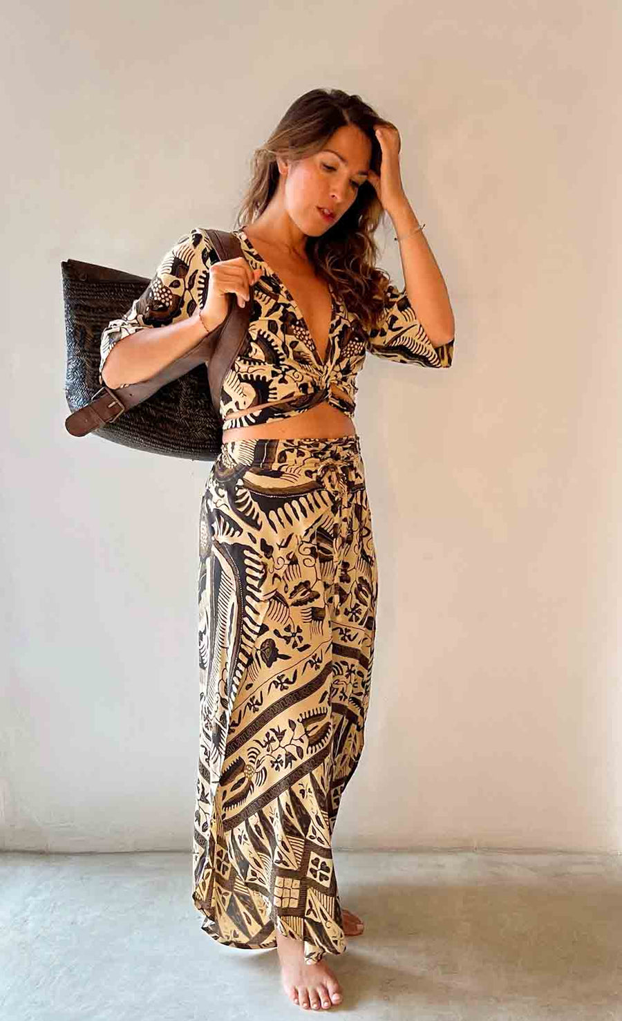 Woman wearing a patterned outfit holding a bag against a plain background