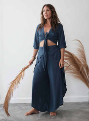 Woman wearing a blue outfit holding a dried plant against a white wall.