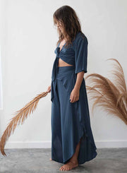 Woman wearing a blue outfit holding a dried plant against a white wall.