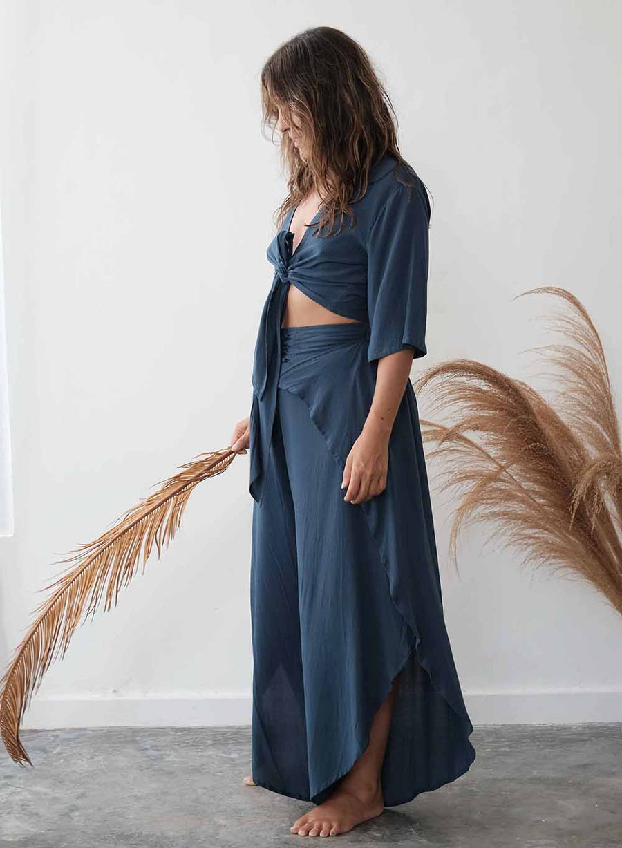 Woman wearing a blue outfit holding a dried plant against a white wall.