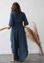 Person wearing a blue jumpsuit standing in front of a white wall with decorative plants.
