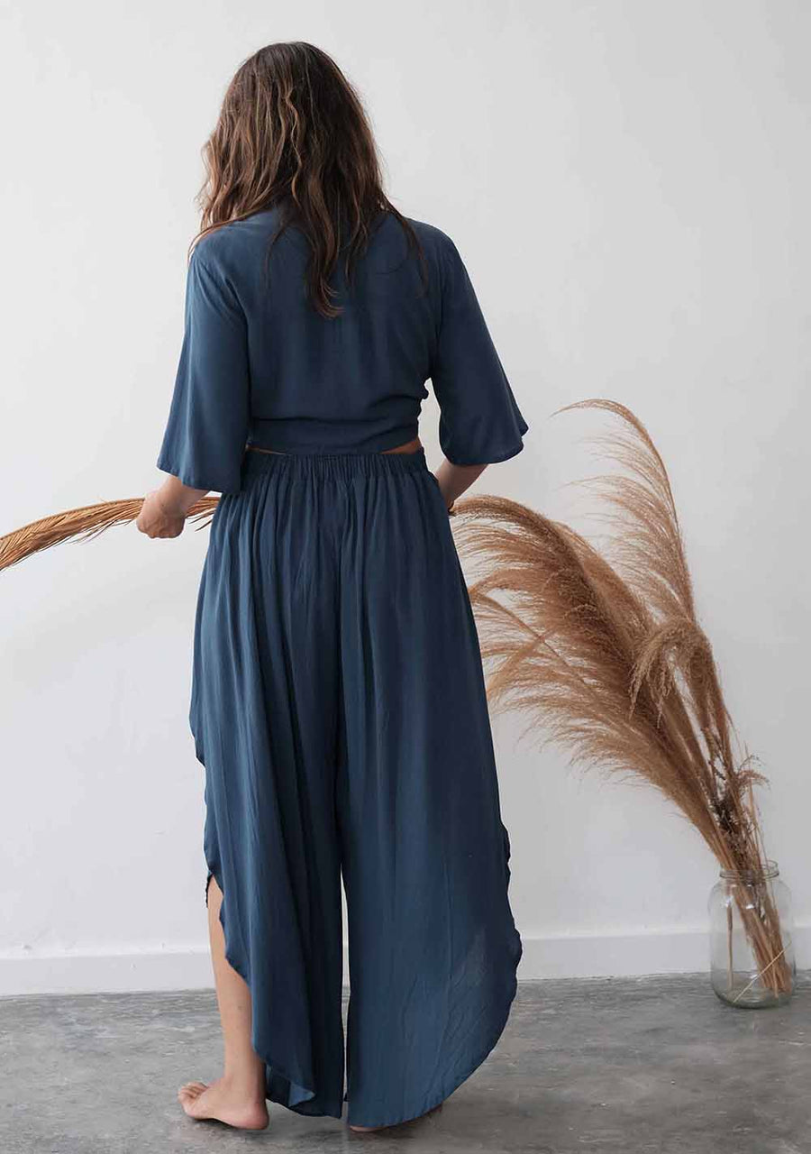 Person wearing a blue jumpsuit standing in front of a white wall with decorative plants.