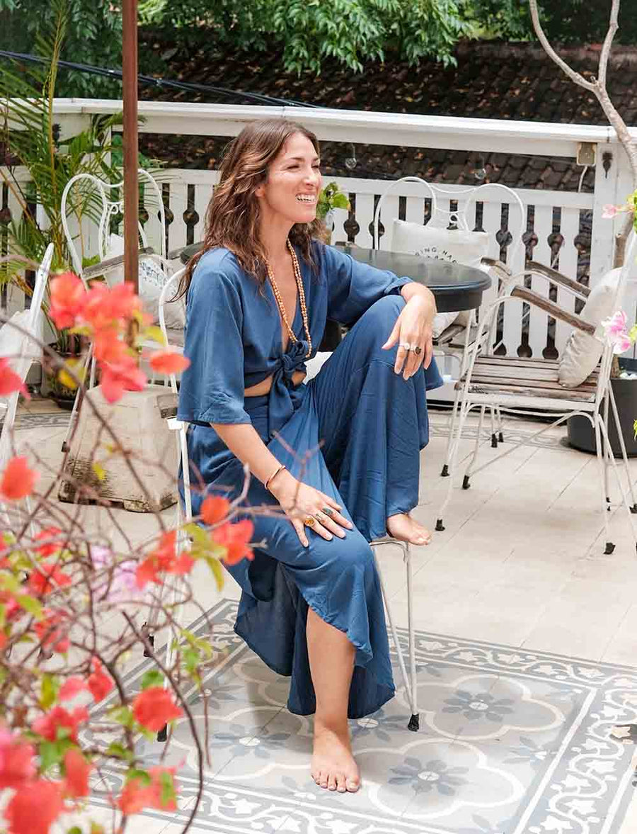 Woman in a blue dress sitting on a chair with flowers and a patio in the background