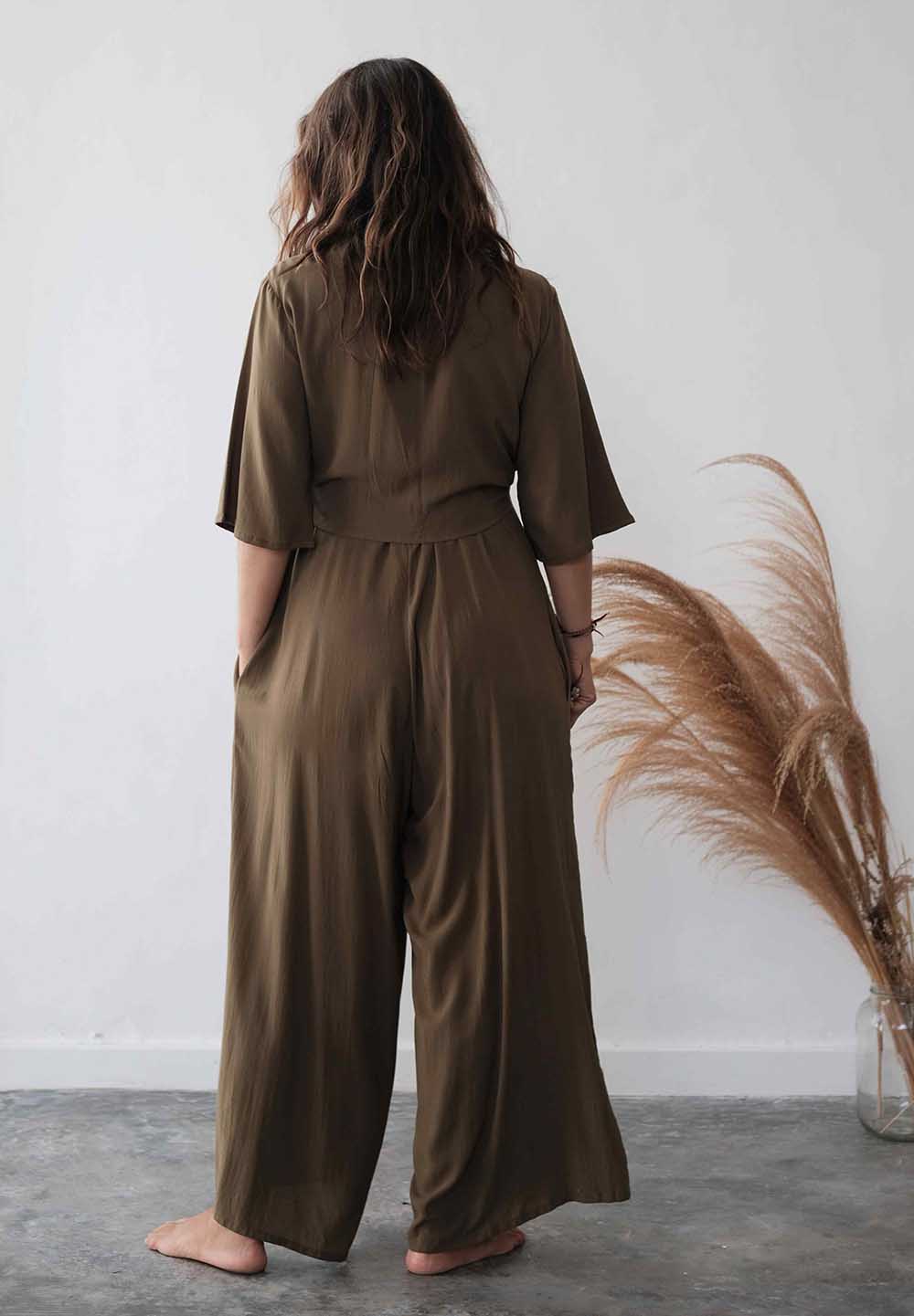 Person wearing a brown jumpsuit standing against a white wall with decorative elements.