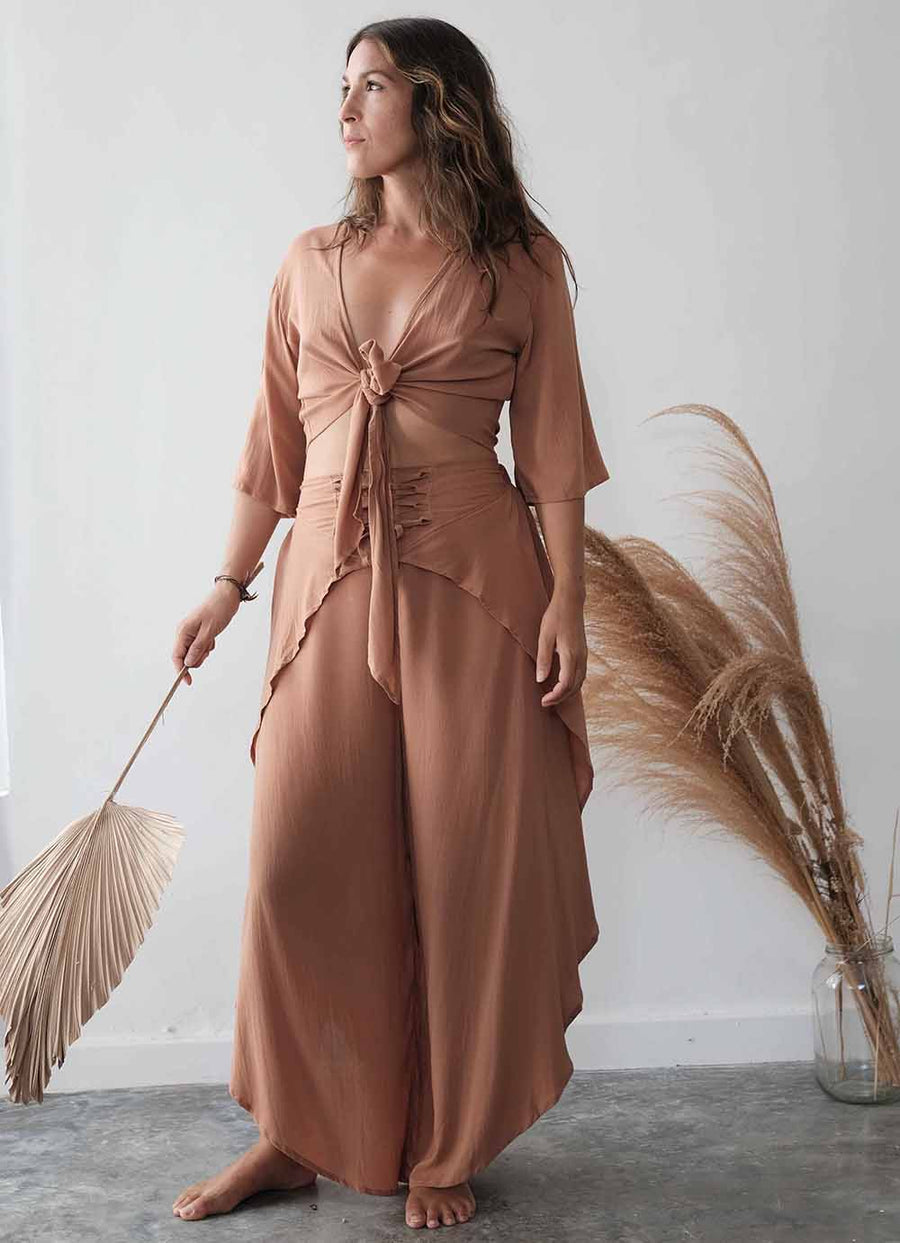 Woman in a brown dress holding a dried plant against a white wall