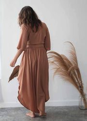 Woman wearing a brown dress standing in a room with pampas grass.