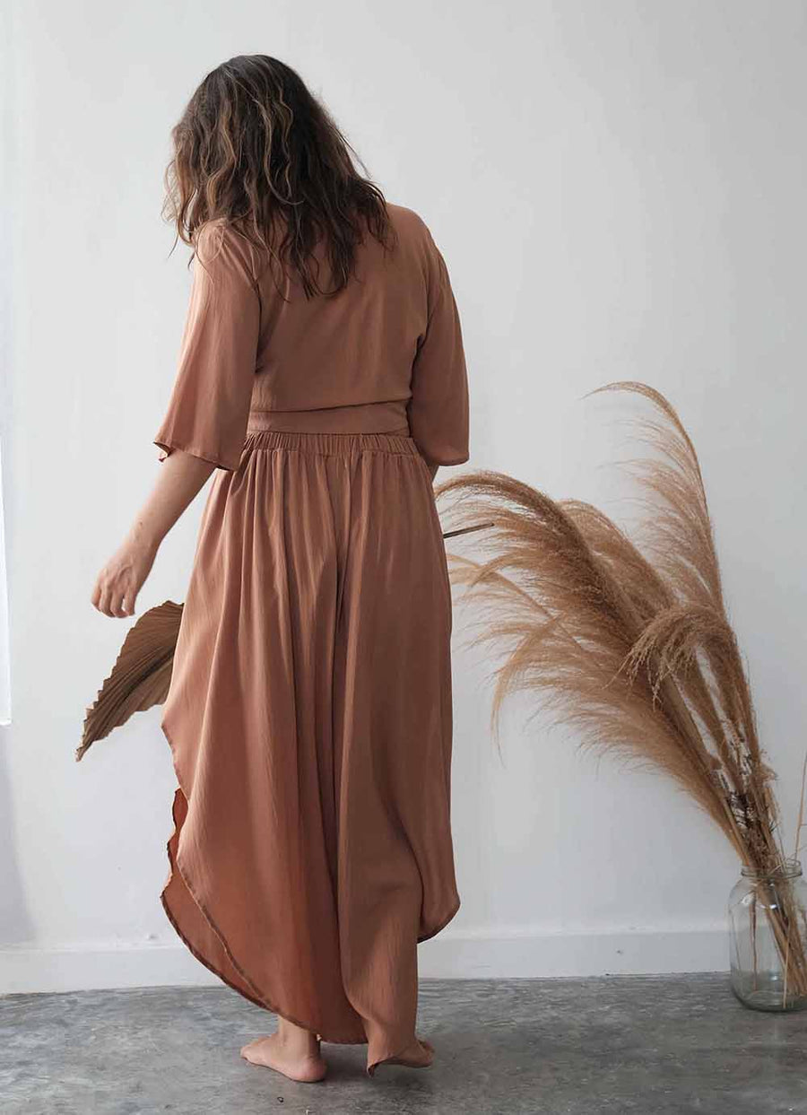 Woman wearing a brown dress standing in a room with pampas grass.