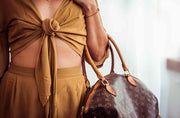 Person wearing a mustard yellow outfit with a brown handbag featuring a logo.