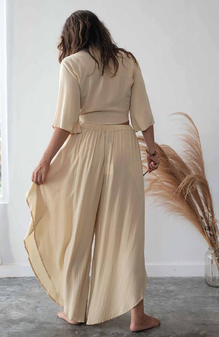 Woman wearing a beige outfit standing in a minimalistic room with a pampas grass plant.