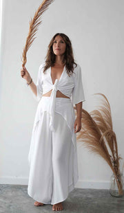 Woman in a white outfit holding dried pampas grass against a plain background