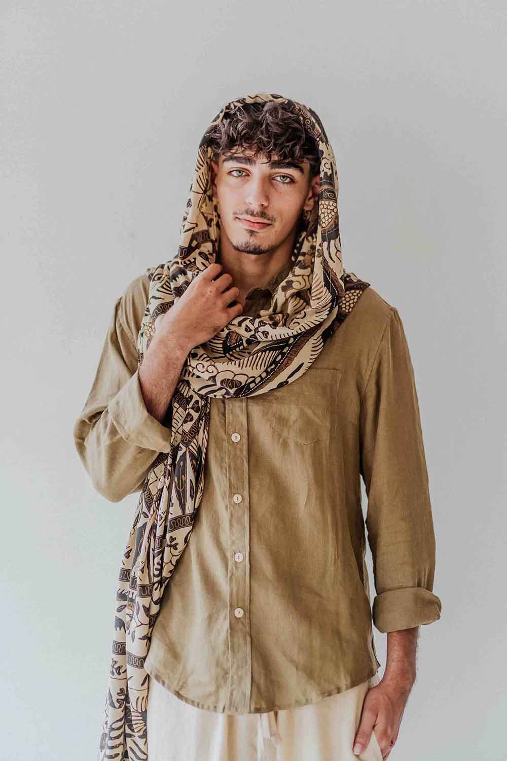 Man wearing a patterned scarf and beige shirt against a plain background