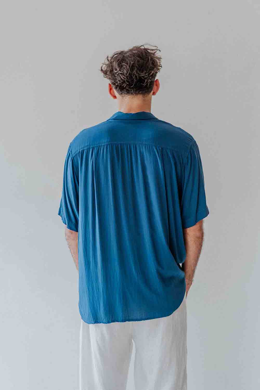 Person wearing a blue shirt and white pants against a plain background