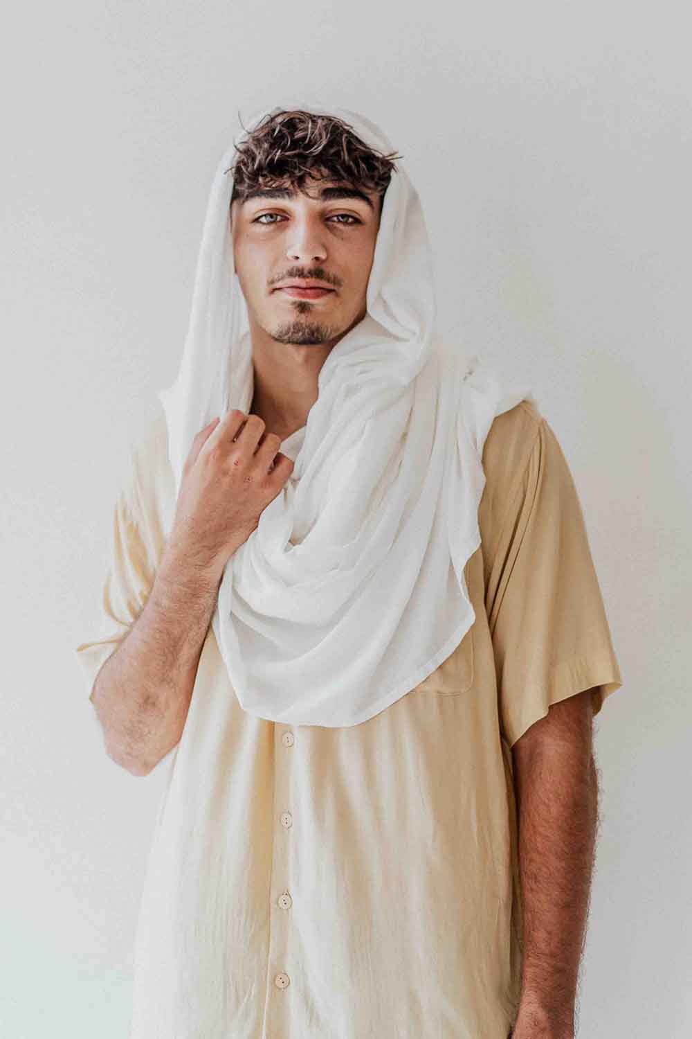 Man wearing a white scarf over his head against a plain background
