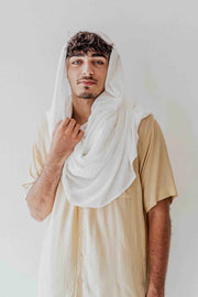 Man wearing a white scarf over his head against a plain background