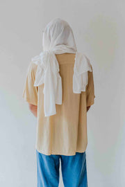 Person wearing a beige shirt and blue pants with a white scarf on a plain background
