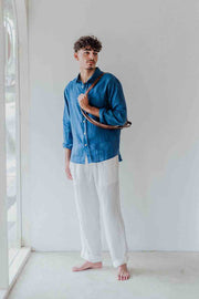 Man wearing a blue shirt and white pants standing in a minimalistic room.