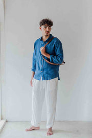 Man wearing a blue shirt and white pants against a plain background
