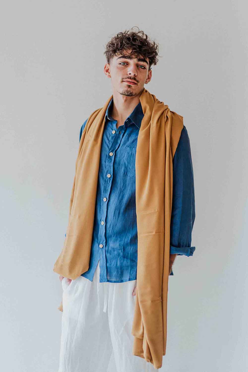 Man wearing a blue shirt and beige vest against a plain background