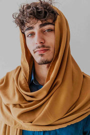 Man wearing a mustard-colored headscarf against a plain background