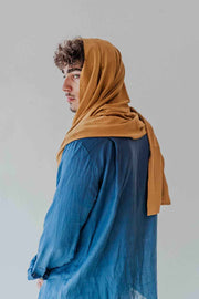 Person wearing a mustard hijab and blue outfit against a plain background