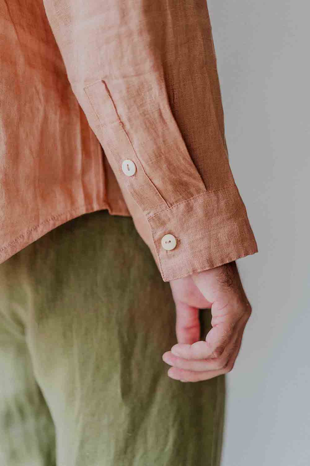 Person wearing a brown shirt and green pants with a neutral background