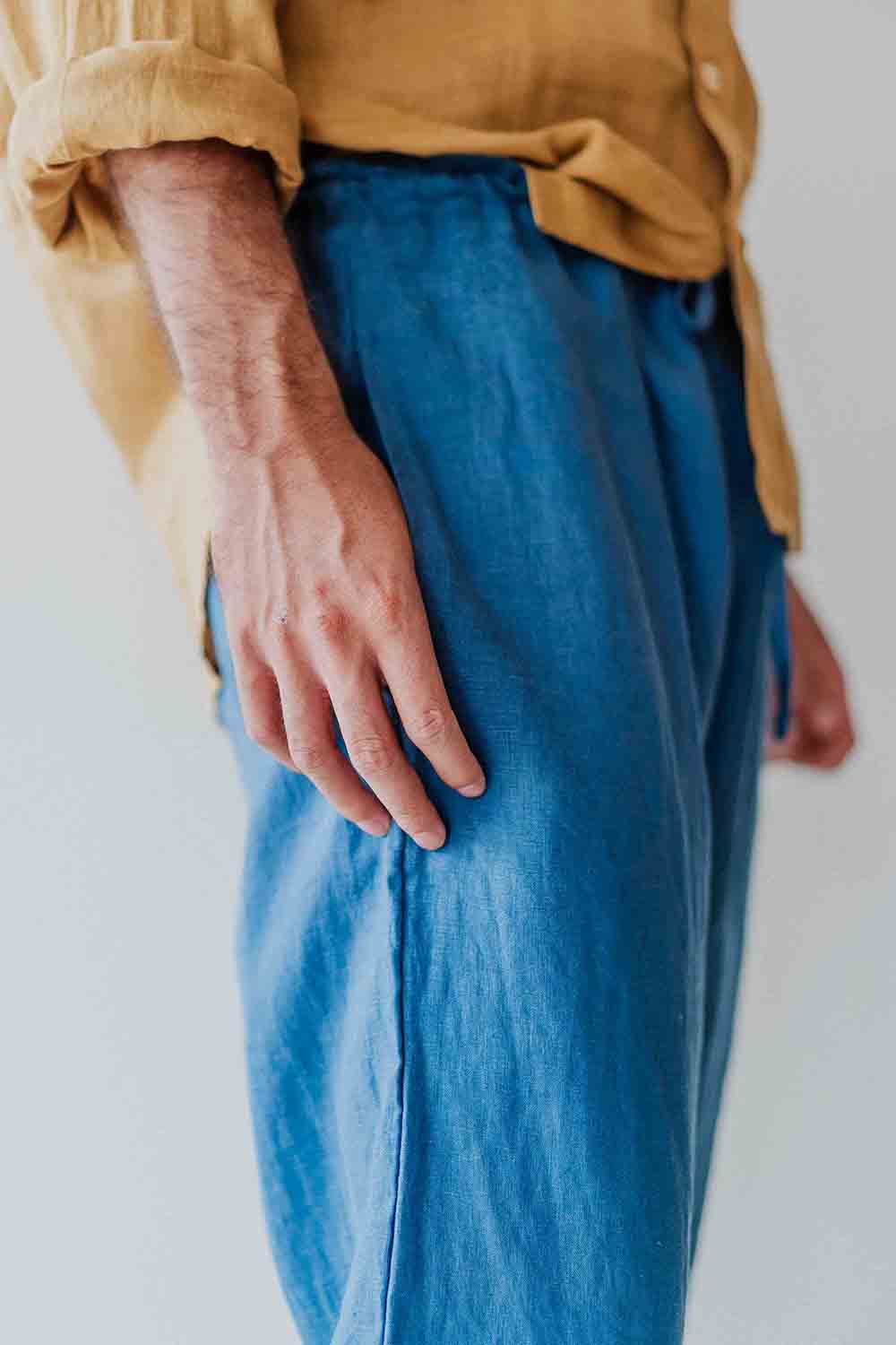 Person wearing a mustard yellow shirt and blue pants against a white background